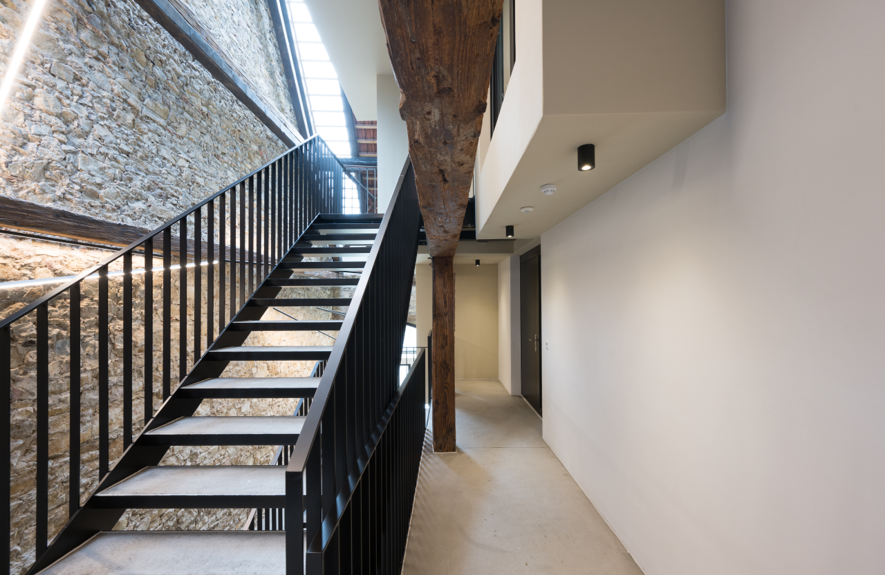 Moderne Treppe mit schwarzem Geländer neben einer Steinwand und Flur in hellem Raum