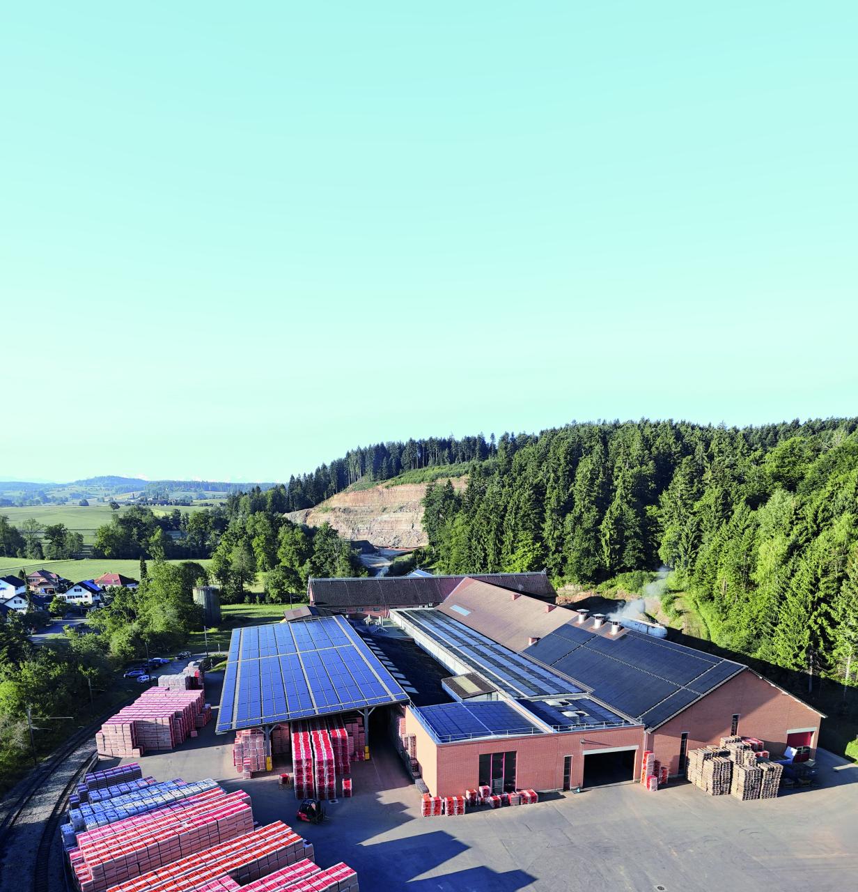 Fabrik mit Solaranlage auf dem Dach, umgeben von Wald und Feldern bei klarem Himmel