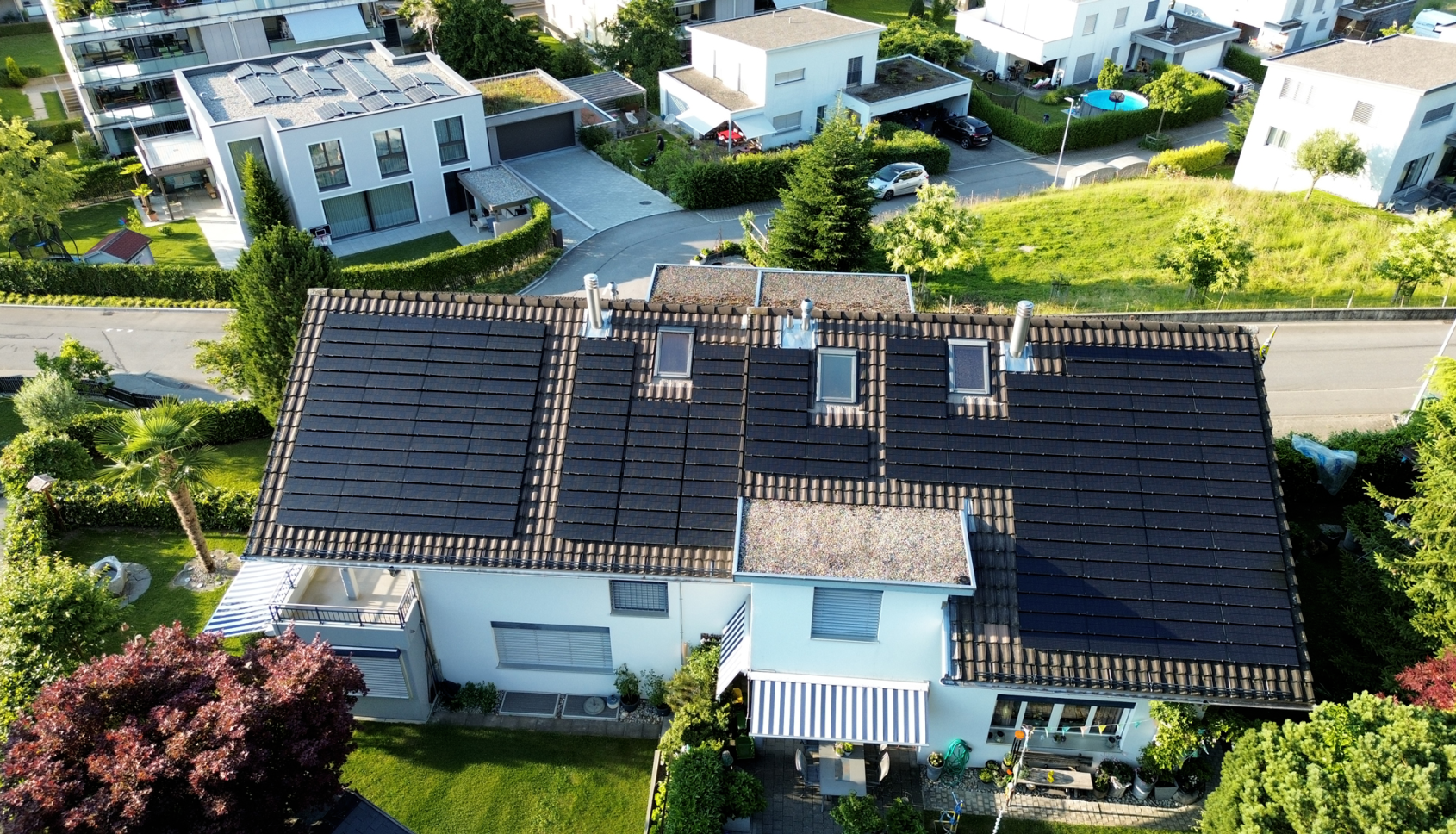 Modernes Einfamilienhaus mit Solarpanelen auf dem Dach, umgeben von Gruen.