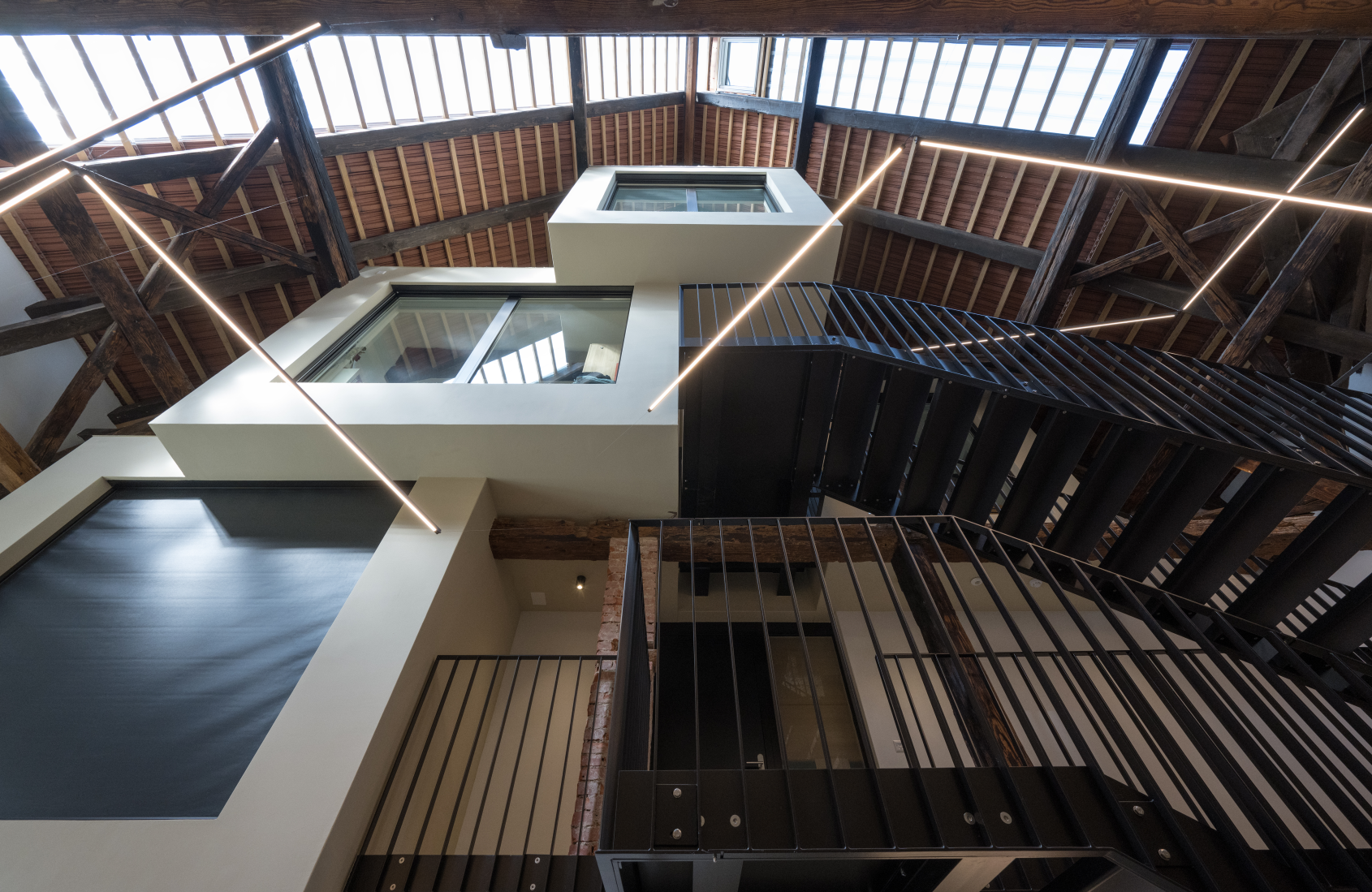 Modernes Treppenhaus mit Glasdach, sichtbaren Balken und geometrischen Strukturen